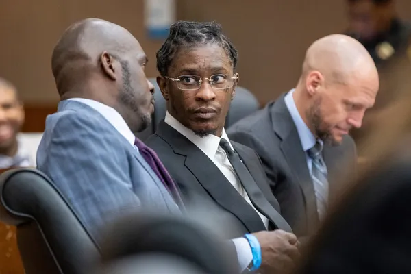 Young Thug, wearing a suit and glasses, looking over at his lawyer during the YSL trial